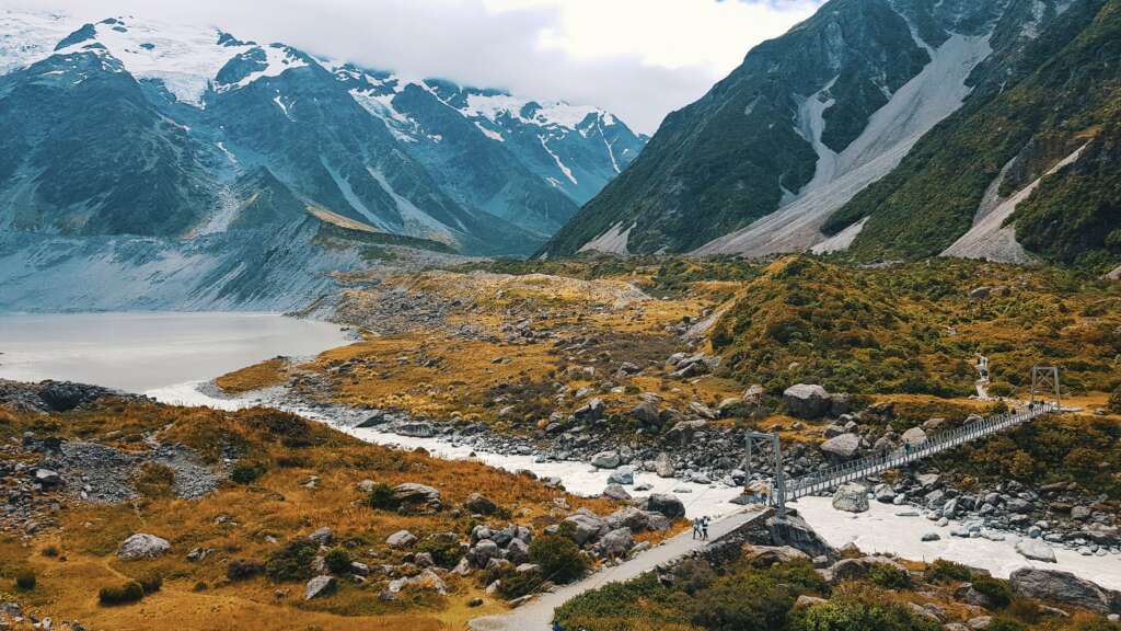 A breathtaking view of Hooker Valley with snowy peaks, rugged terrain, and a suspension bridge in Mt Cook National Park.